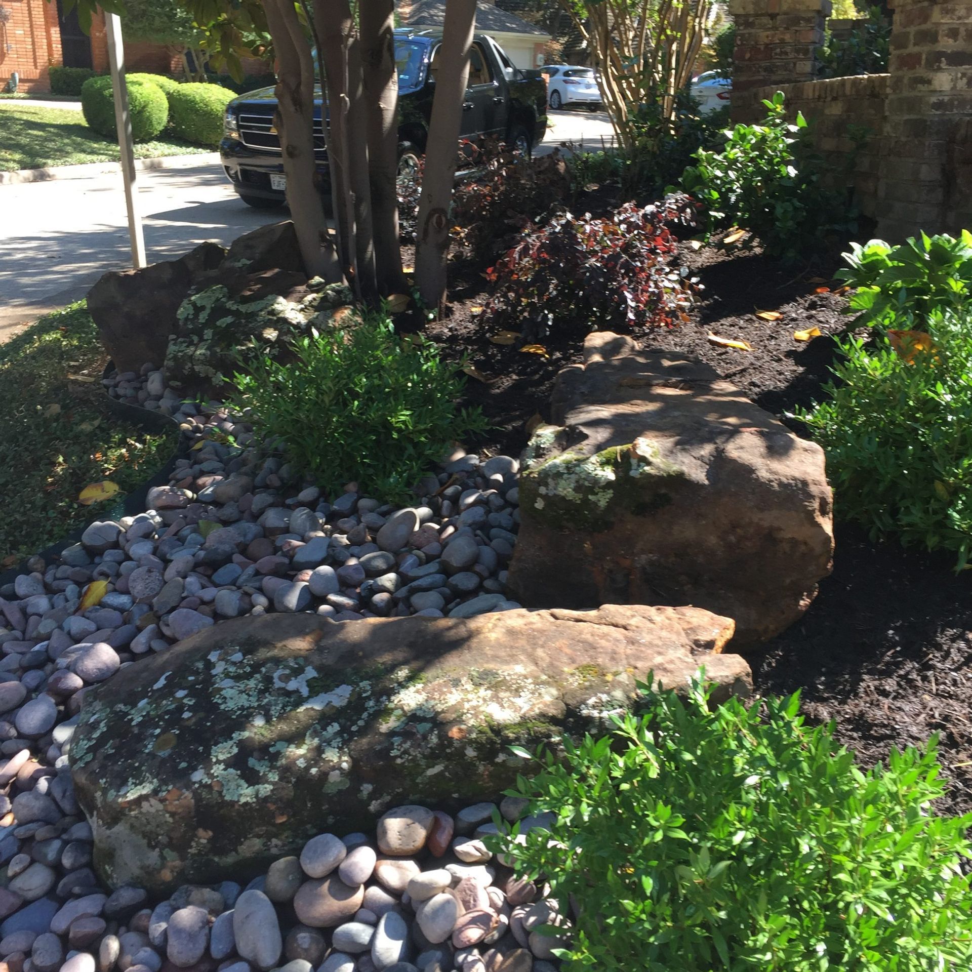 Landscaped front yard with large rocks, gray pebbles, and various green shrubs.