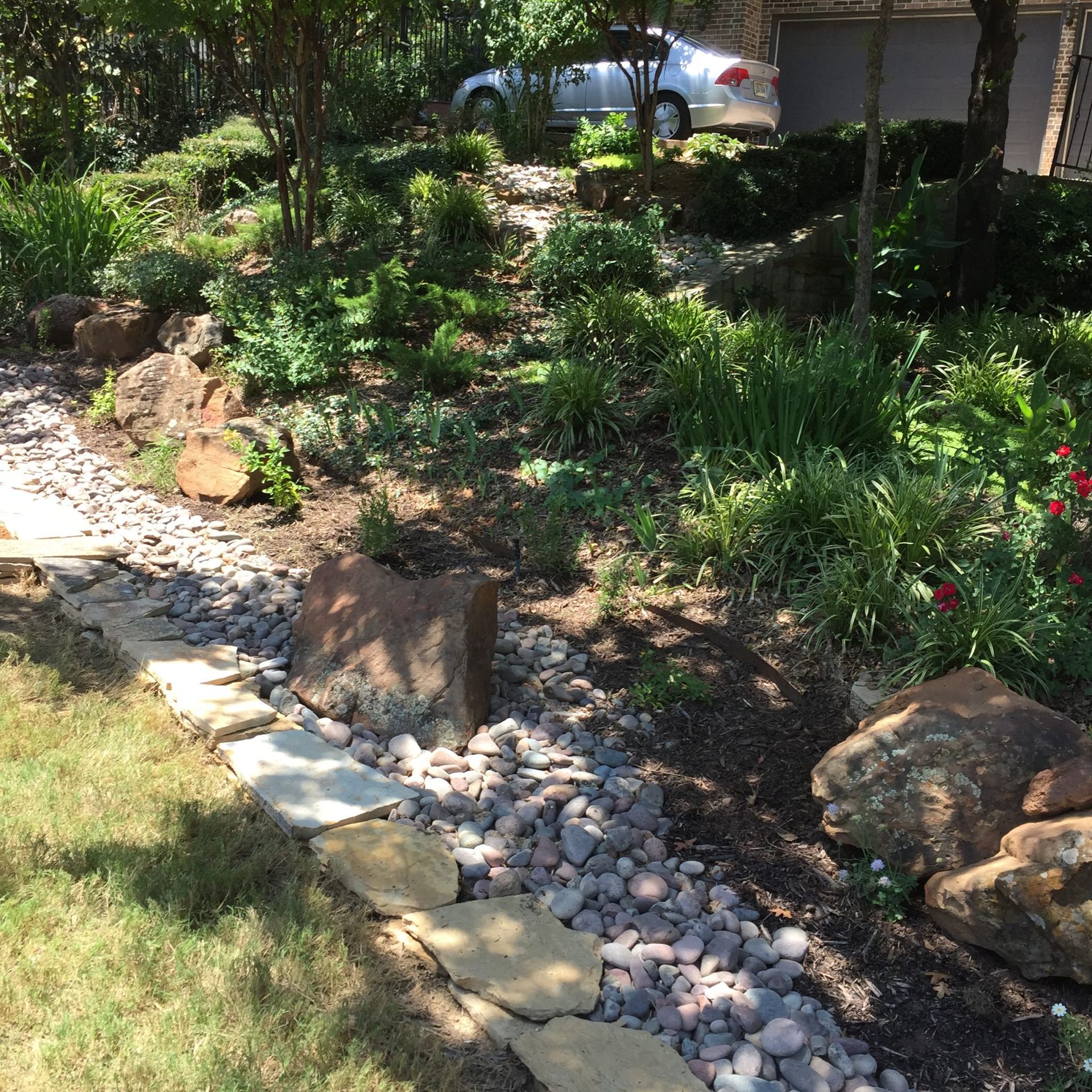 Stone path and bed of plants in a sunny garden, with a car in the background.