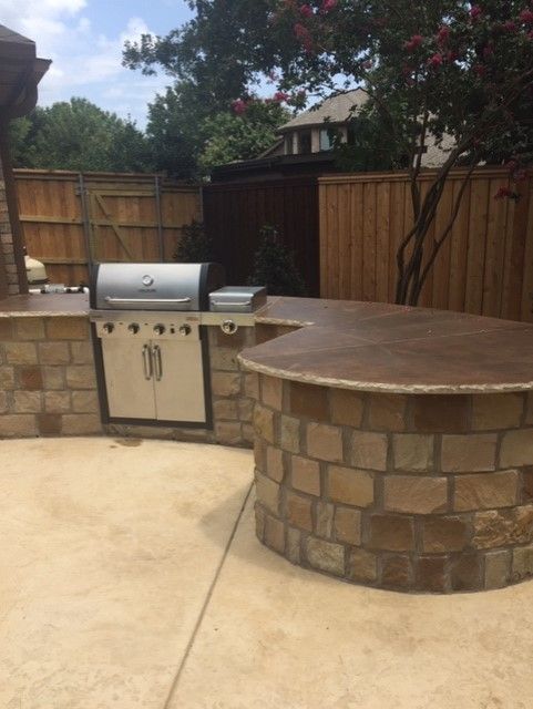 Outdoor kitchen with stone counter and grill. Beige stone structure, brown counter.