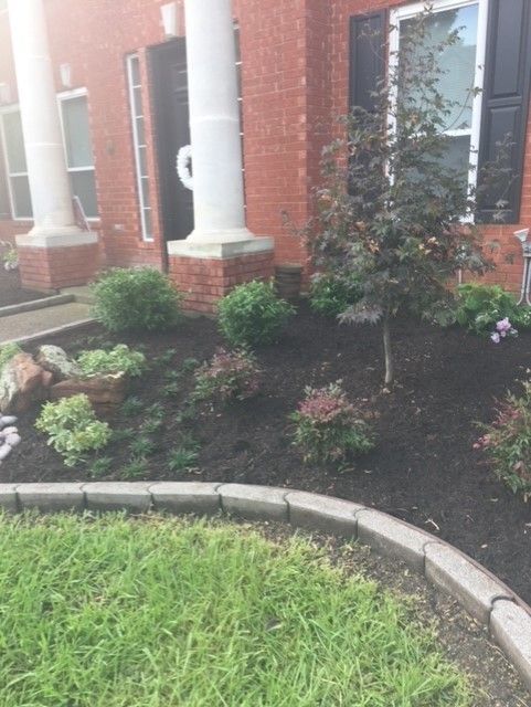 Brick house with landscaped bed; green lawn with stone edging.