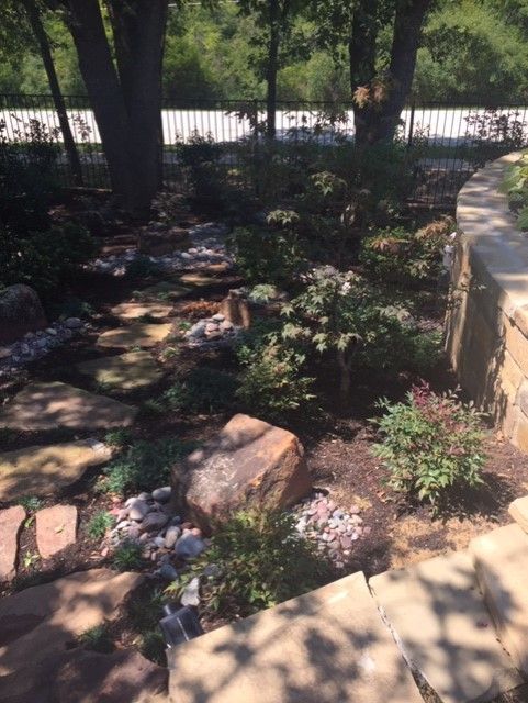 Stone path and garden with rocks, plants, and trees, bordered by a stone wall.