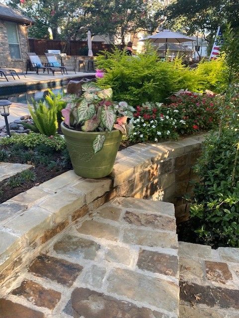 Stone steps lead to a flower garden with a potted plant next to a pool.