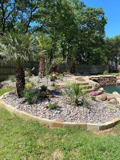 Palm trees and other plants in a rock garden border a pool on a sunny day.