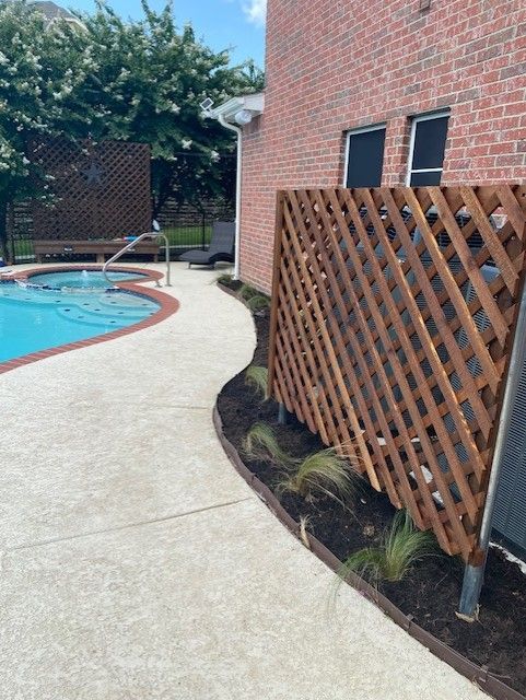 Poolside with lattice fence, brick house, and landscaped border.