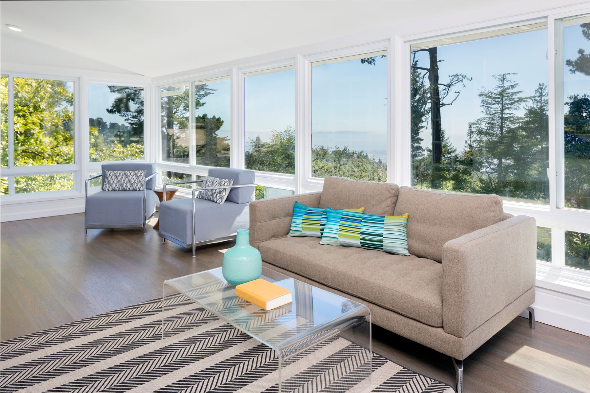 Bright modern living room with beige sofa, glass table, and large windows overlooking trees