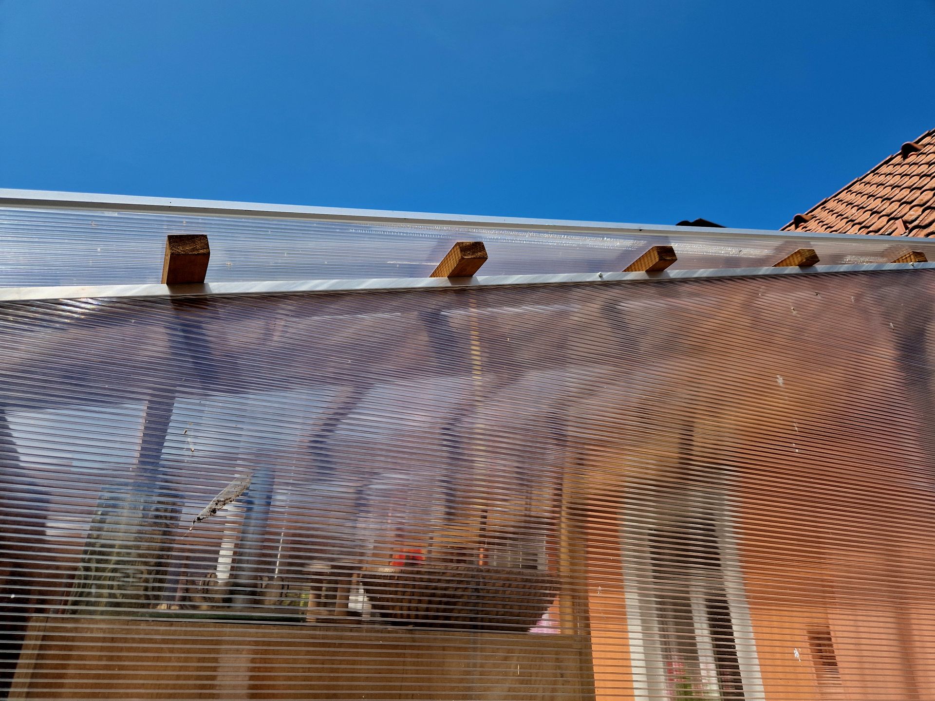 Transparent mesh covering a brick house exterior under a blue sky, with roofline and windows visible