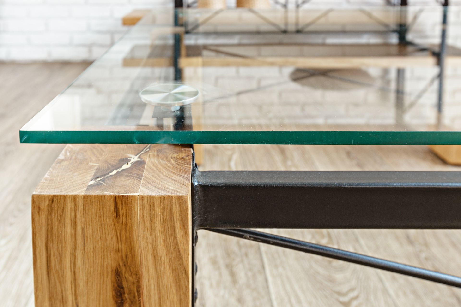 Close-up of a glass tabletop with a wooden leg and black metal support on a light wood floor.