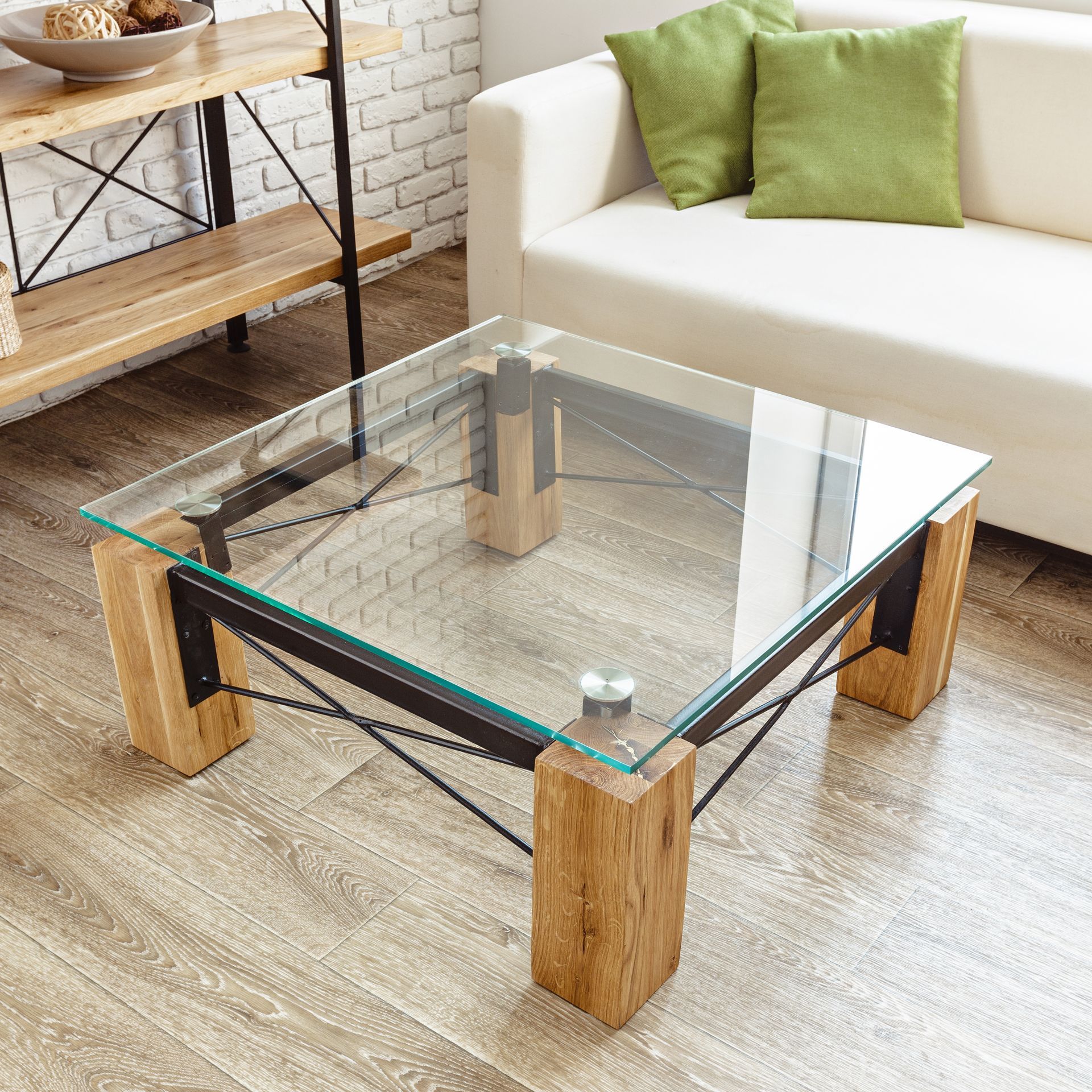 Glass coffee table with wooden legs in a bright living room beside a white sofa and green pillows