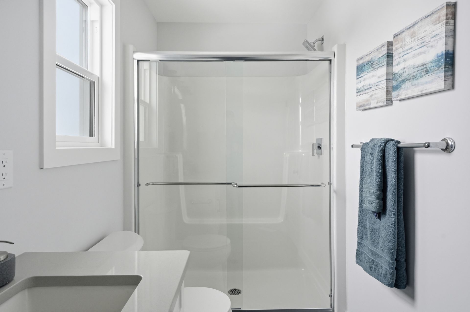 Bright white bathroom with glass shower, sink, towel rack, and wall art.