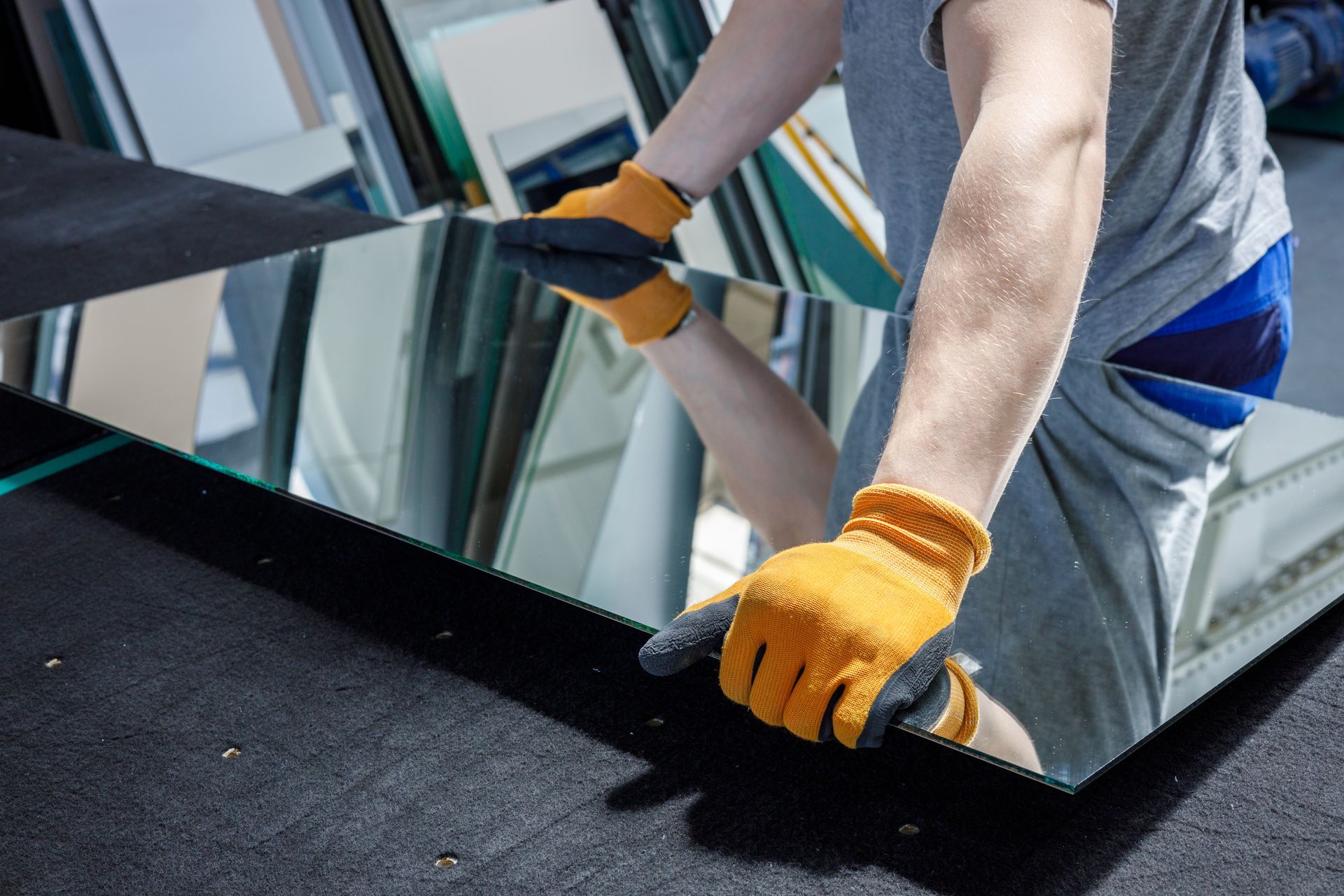 Worker in orange gloves installing a large glass pane on a rooftop.