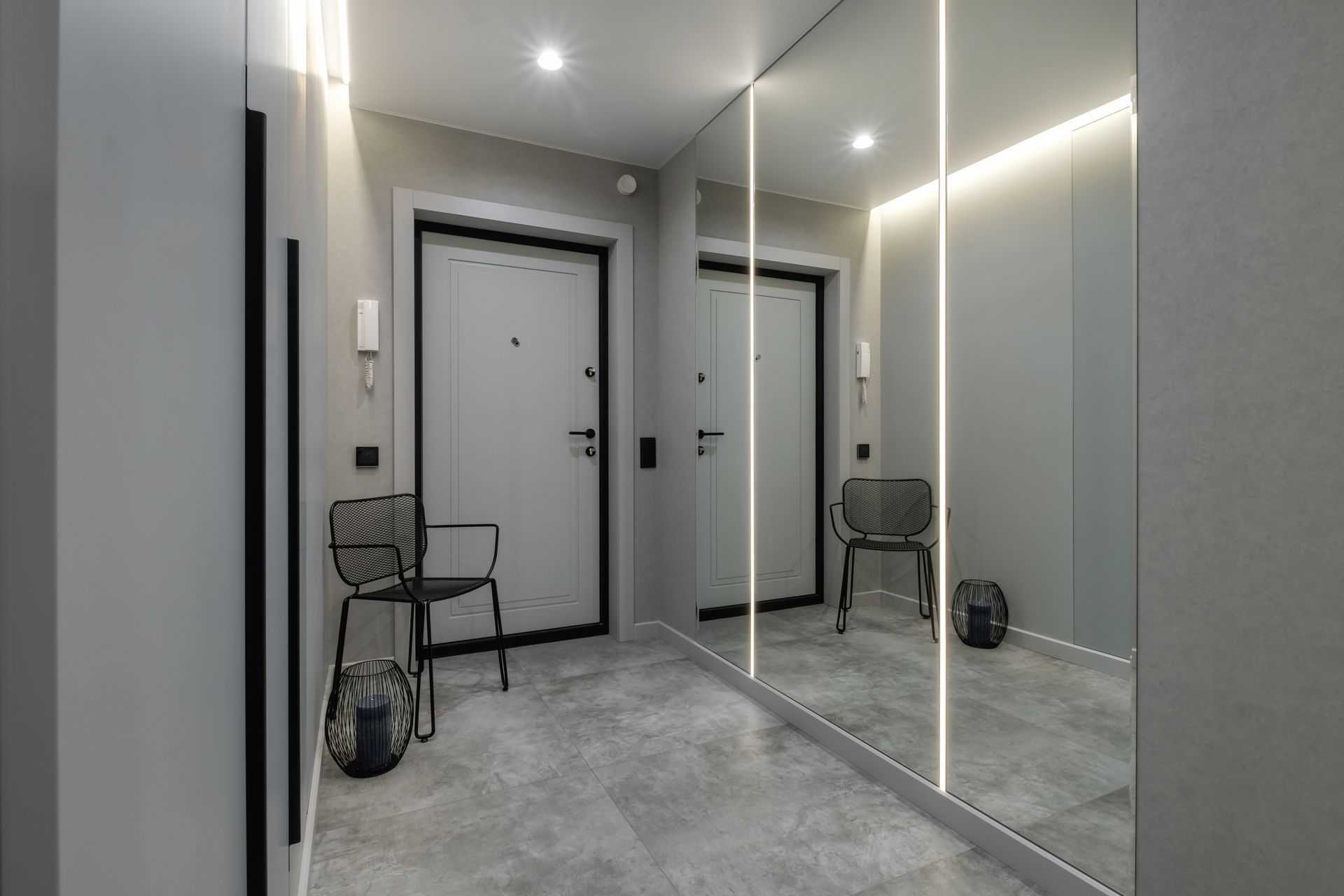 Modern gray hallway with mirrored closet doors, two chairs, and a closed door under recessed lights