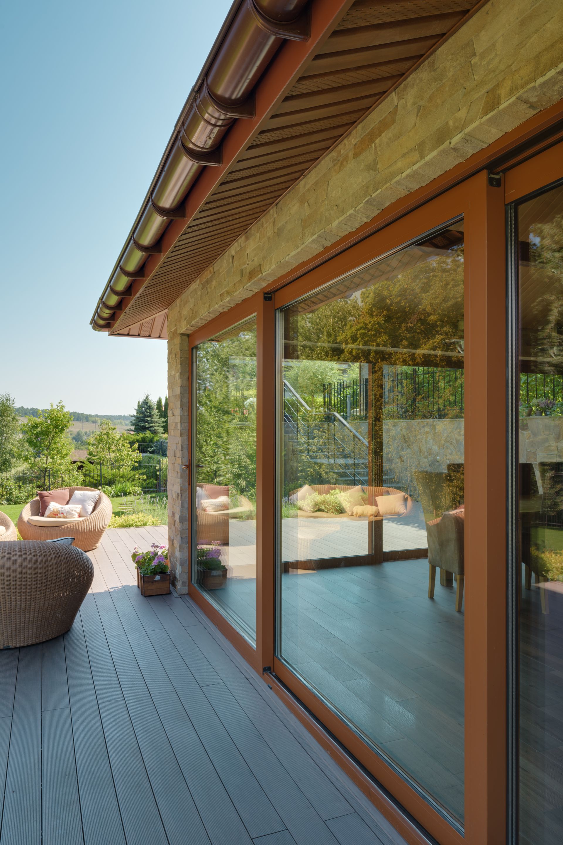 Modern patio with wood deck, glass sliding doors, and a woven chair beside a grassy yard.