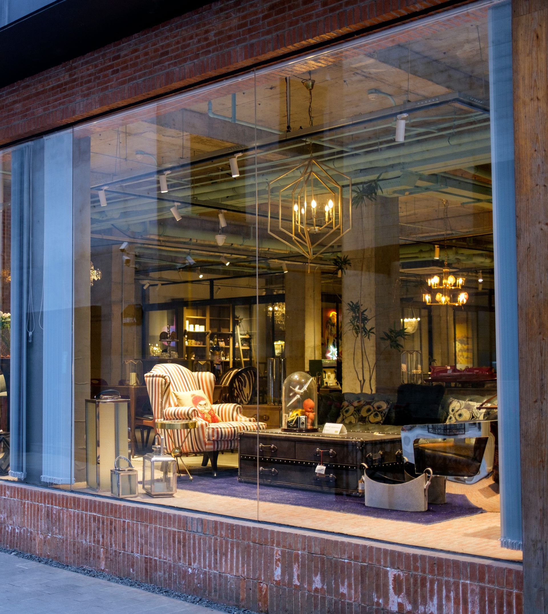 Storefront window display with warm interior lighting, furniture, and mirrors behind glass in a brick building