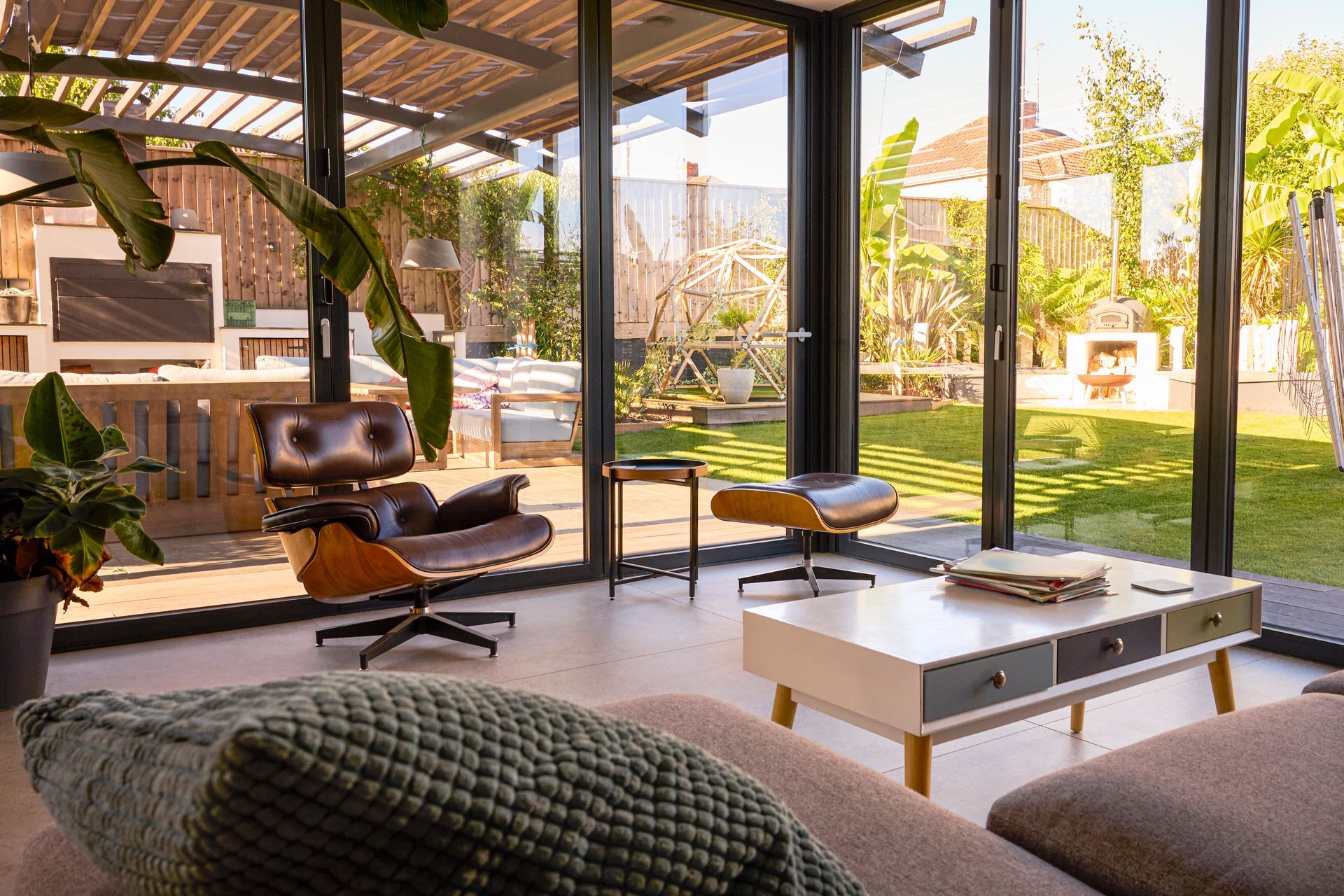 Modern patio living room with lounge chairs, white coffee table, and open view of a sunny garden