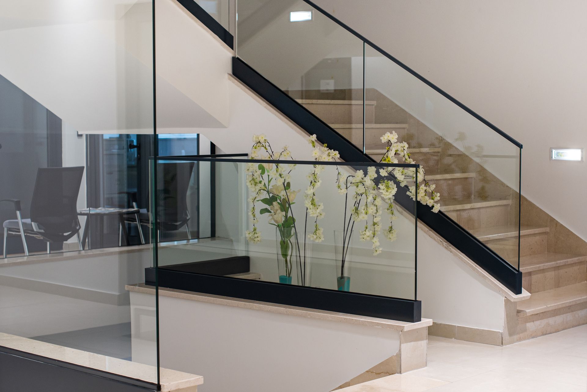 Modern office lobby with glass staircase and indoor plants beside a desk area