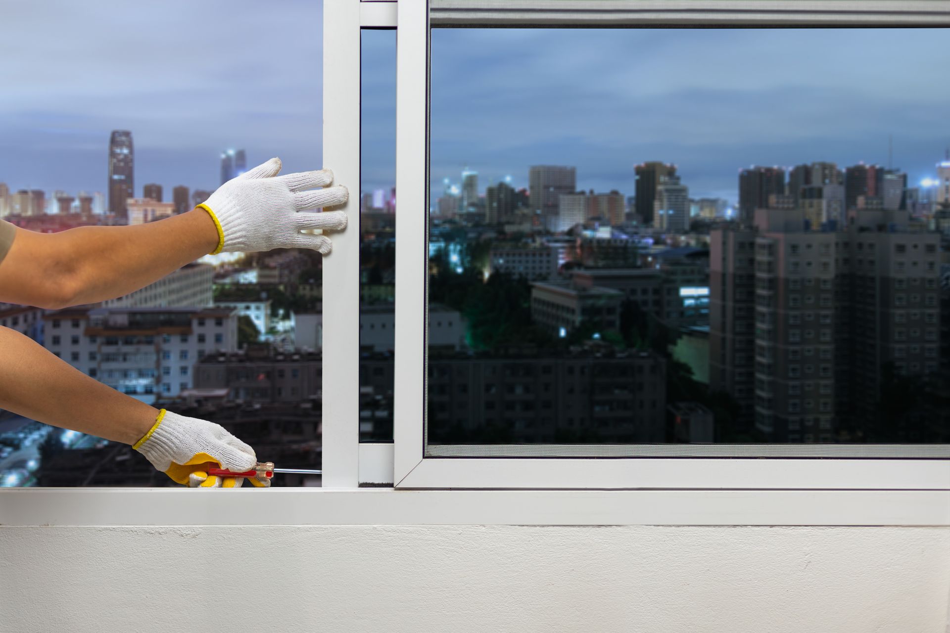 Gloved hands cleaning a city window with a squeegee, skyline reflected in the glass
