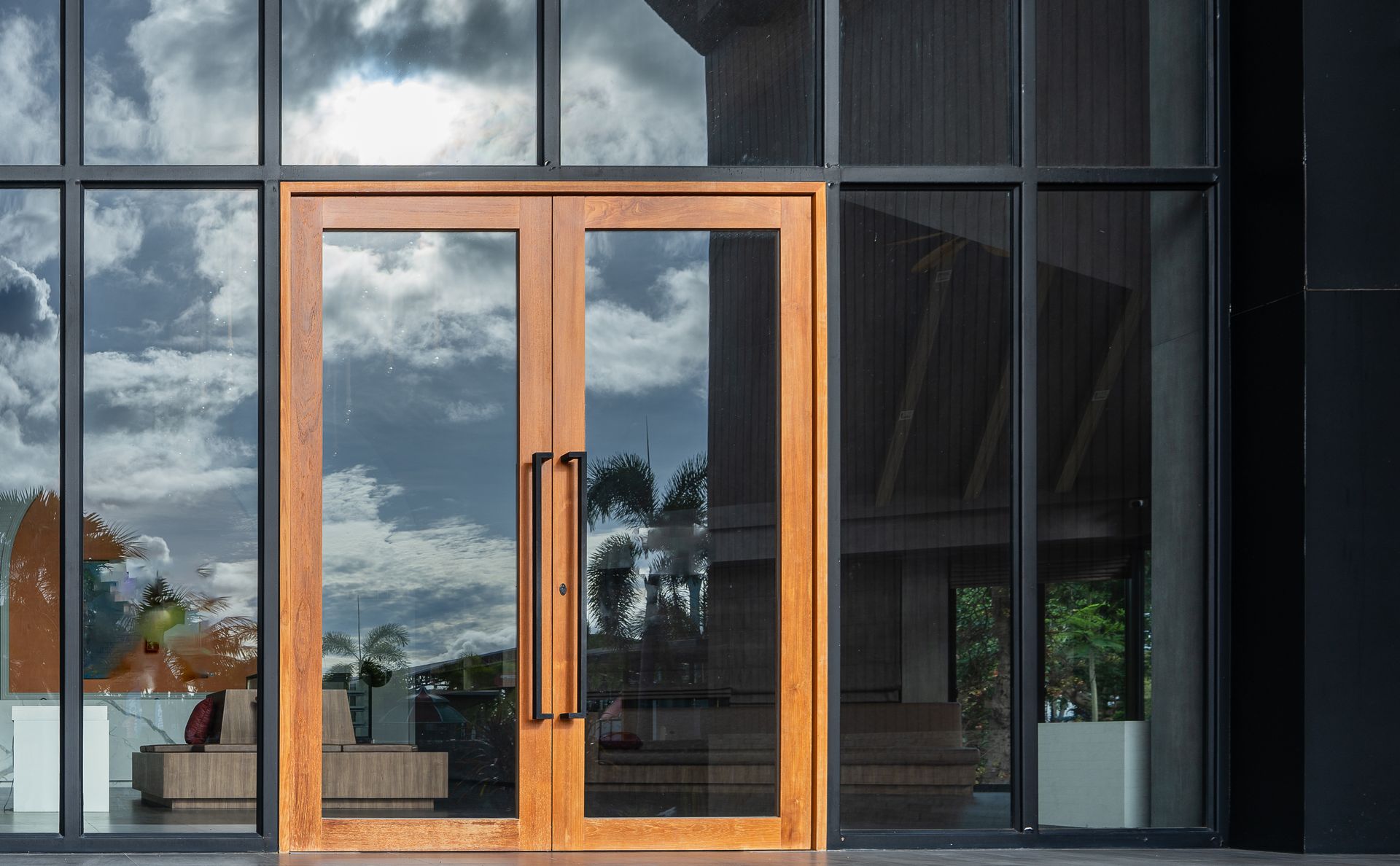 Modern building entrance with wooden double doors and large reflective glass windows.