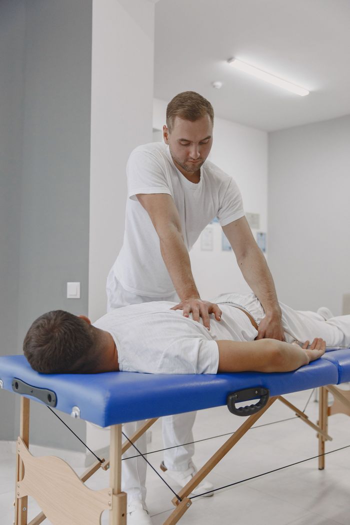 Therapist giving a back massage to a patient on a blue treatment table in a bright clinic room