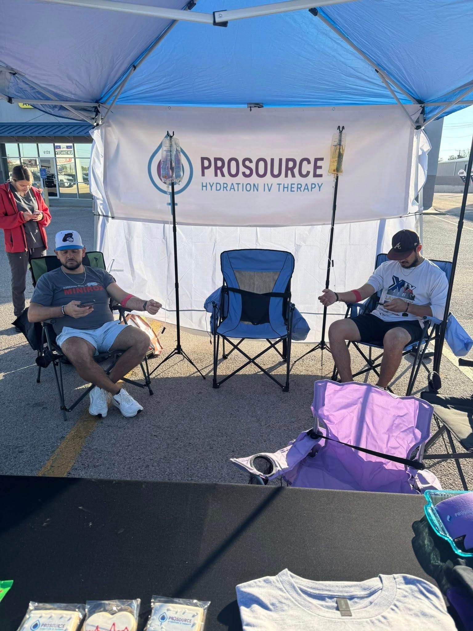 Two men sit at an outdoor booth under a canopy, a banner reading