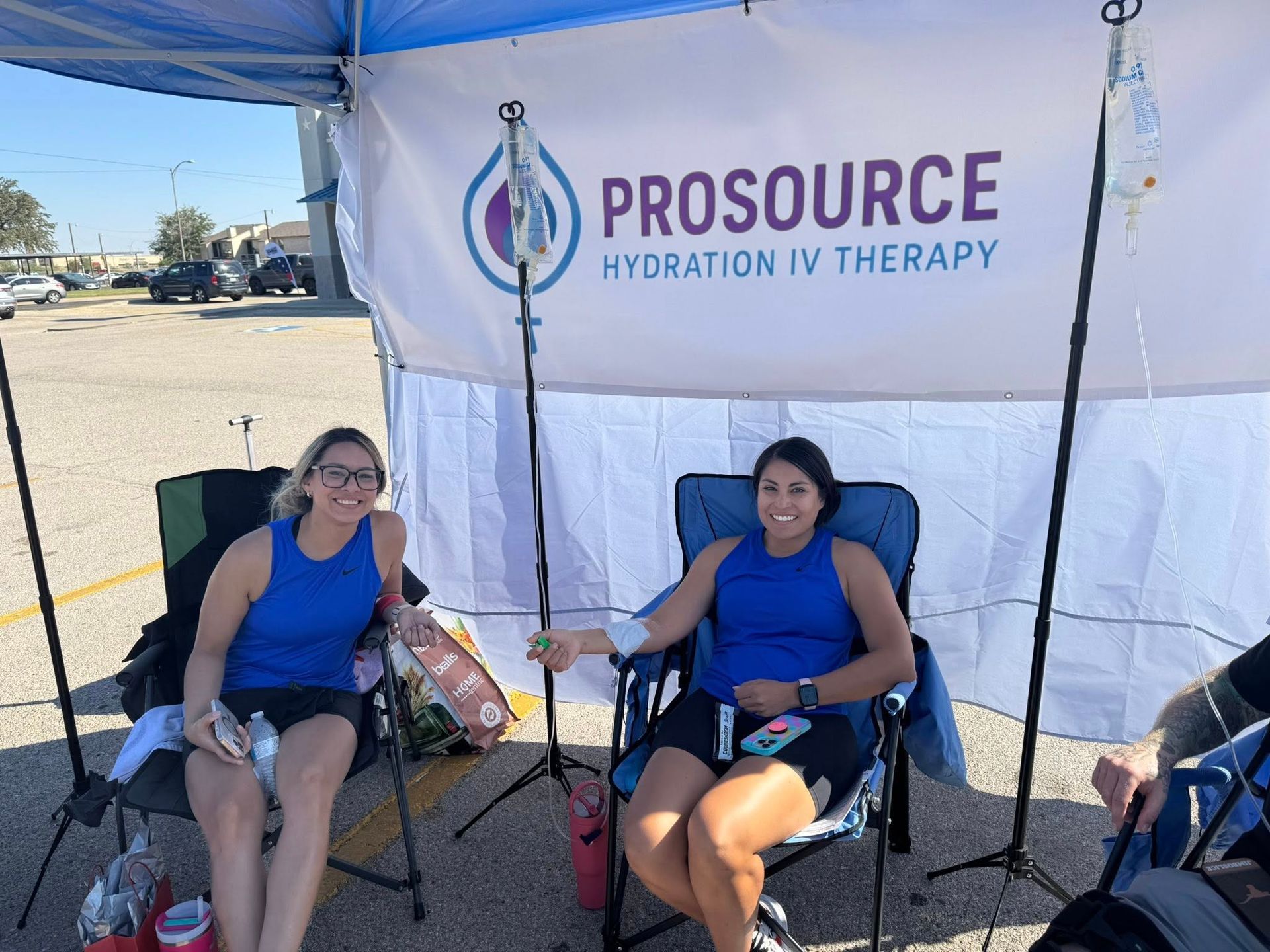 Two women receiving IV hydration therapy under a canopy with