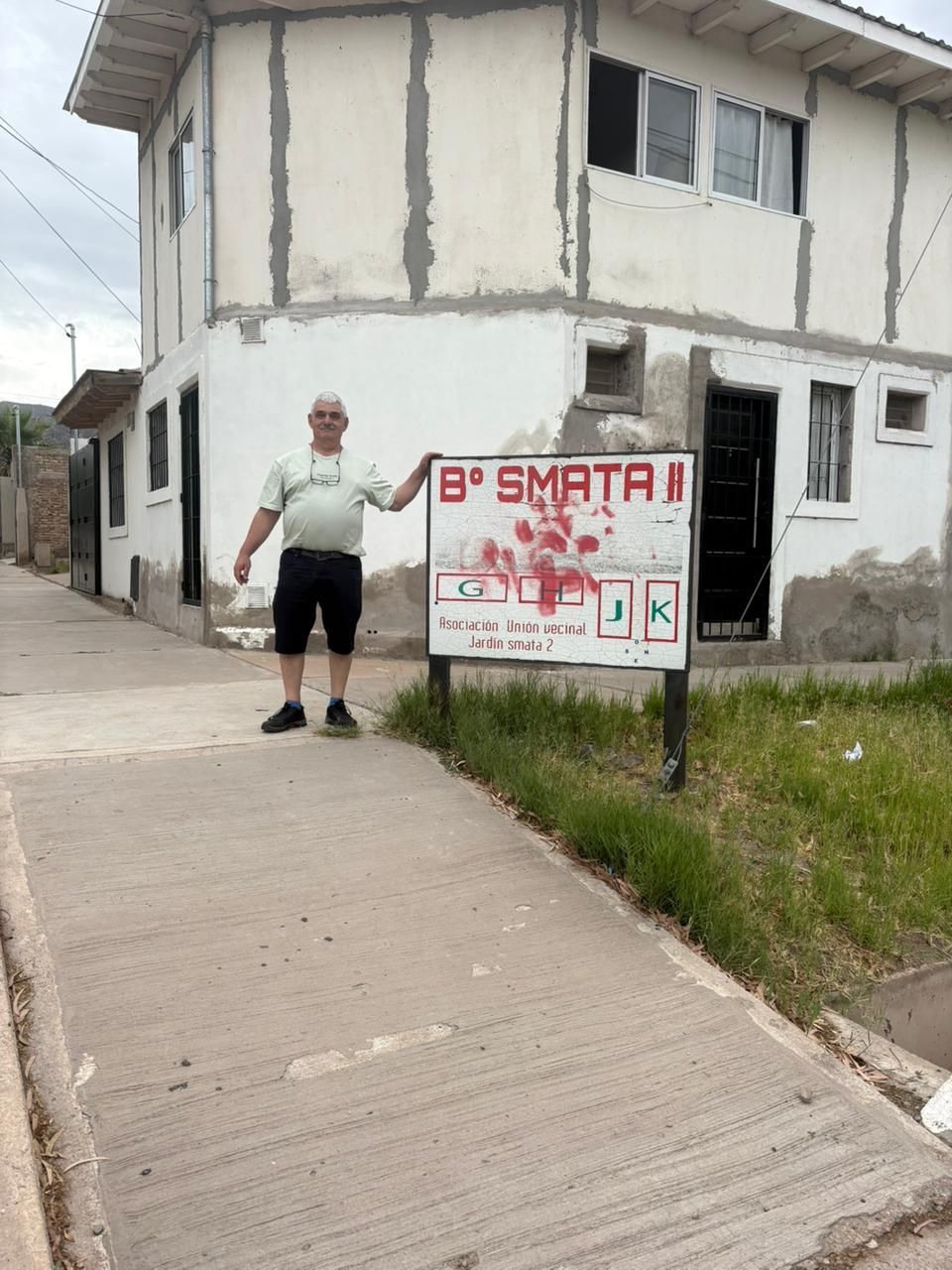 Un hombre señala un letrero frente a un edificio de dos plantas. El letrero dice