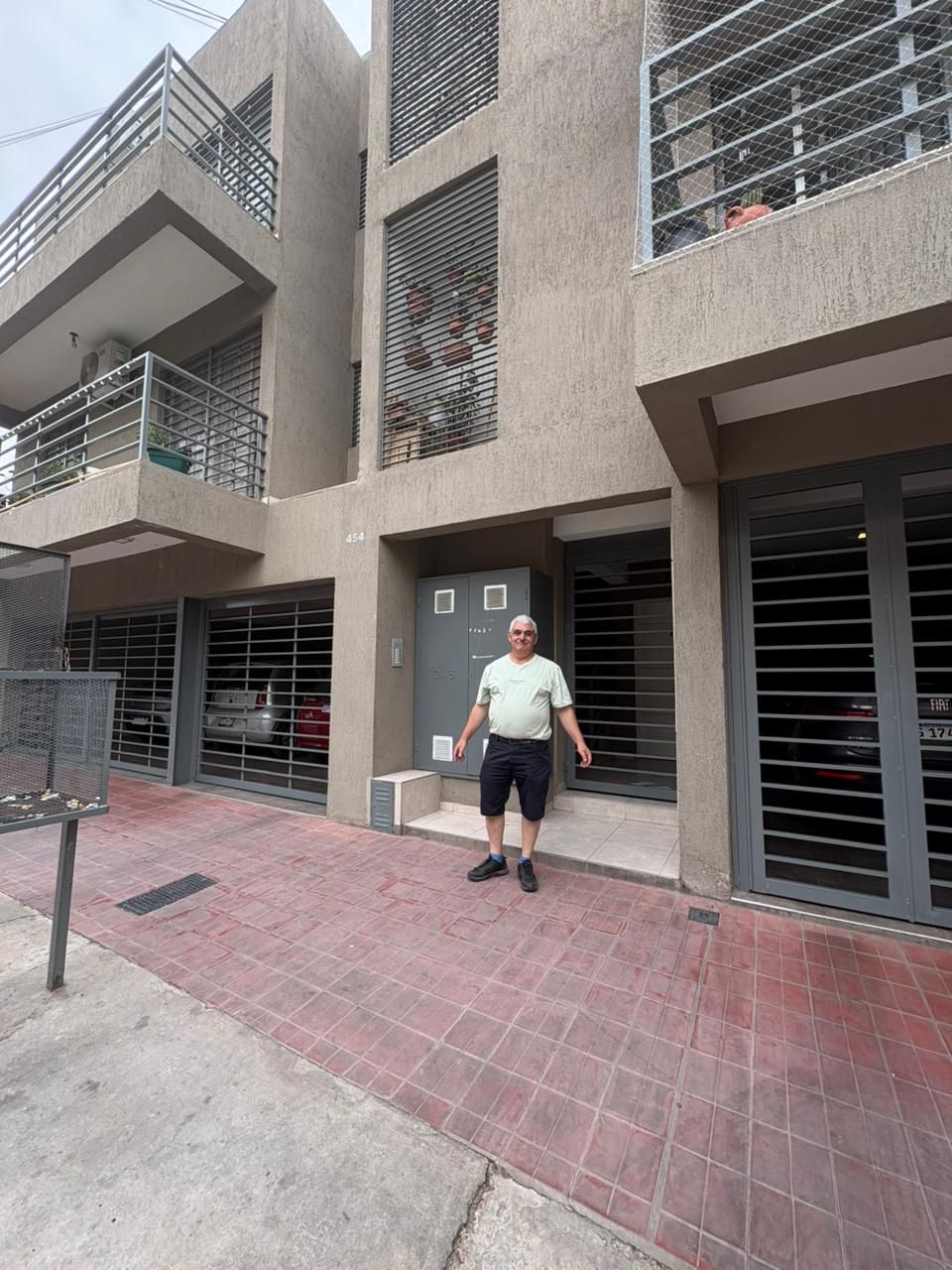 Hombre parado frente a un edificio de tres pisos con rejas de seguridad en ventanas y entradas.