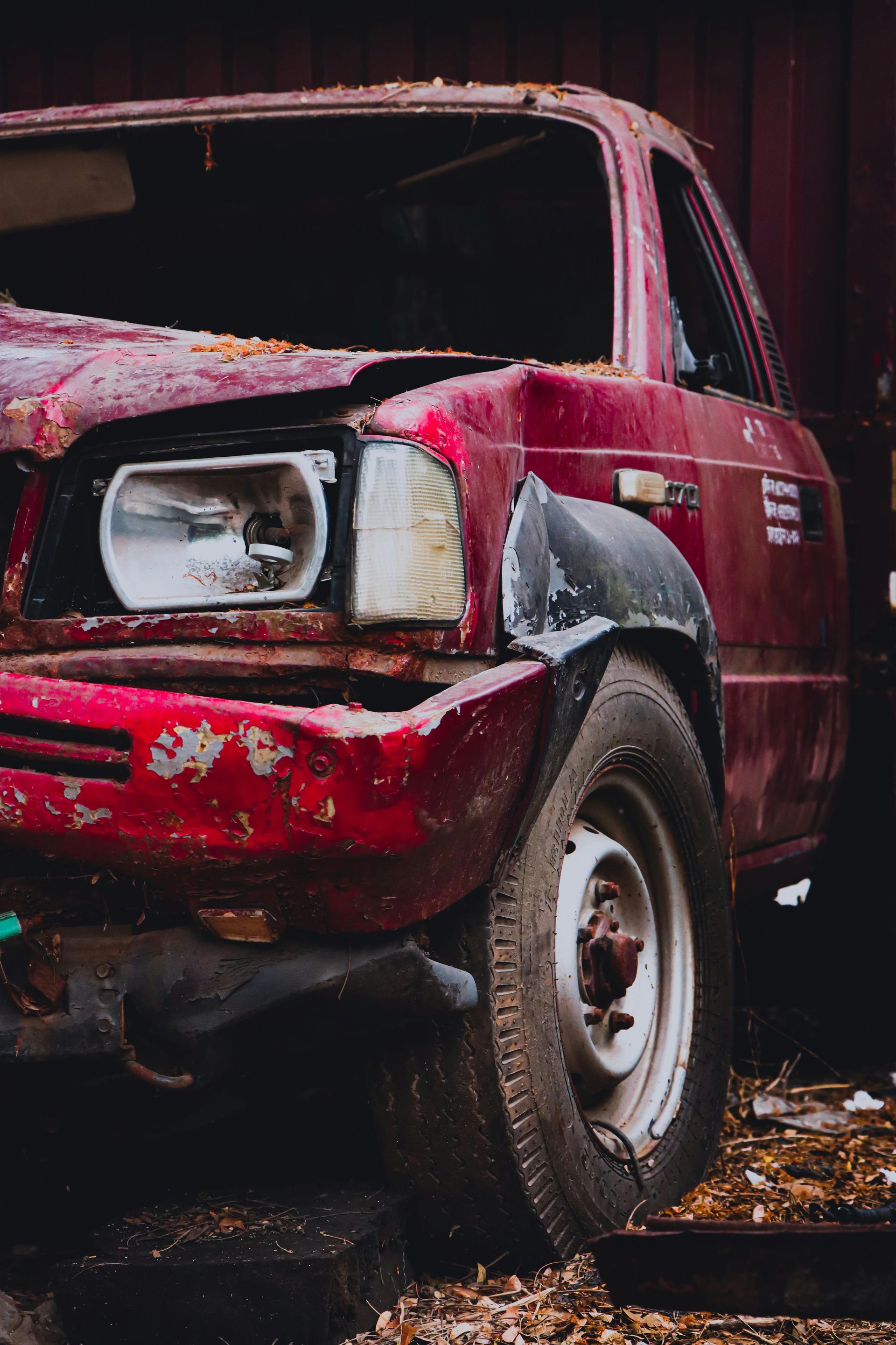 A close-up of a damaged, weathered red truck parked in a scrapyard.