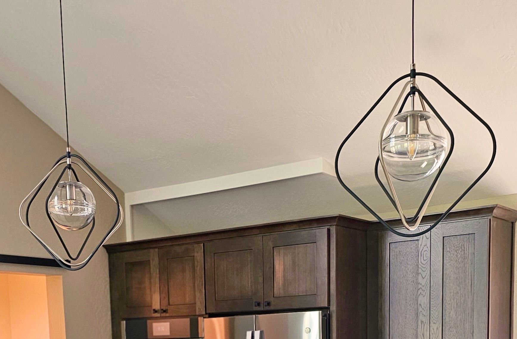Two geometric pendant lights hanging above dark kitchen cabinets.