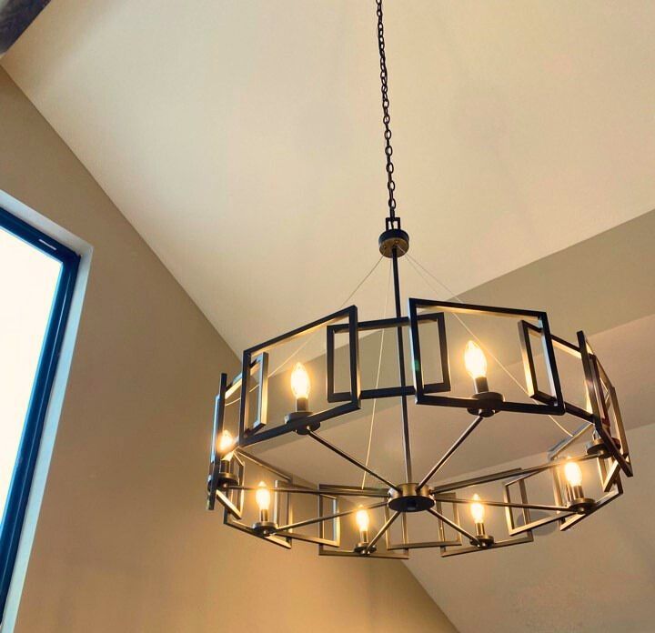 Black metal chandelier with lit candles hanging from a ceiling in a corner room