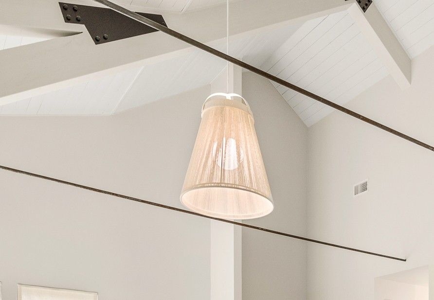 White pendant lamp hanging from a high ceiling with dark support beams