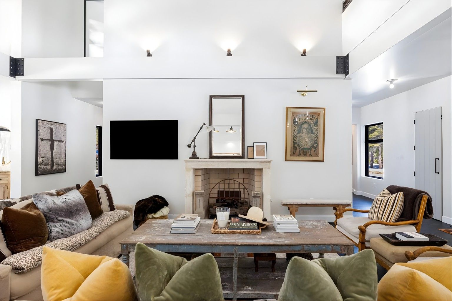 Bright living room with sectional sofas, TV, fireplace, artwork, and high white walls