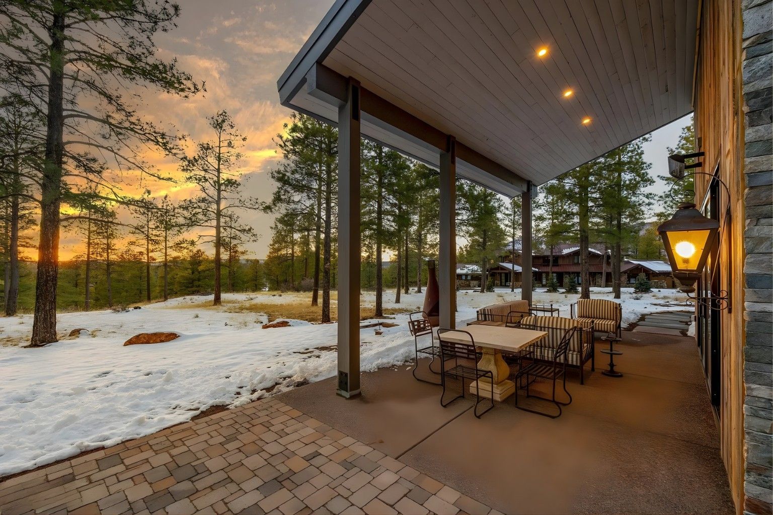 Covered patio overlooking snowy yard at sunset, with outdoor chairs and warm lights glowing under the roof