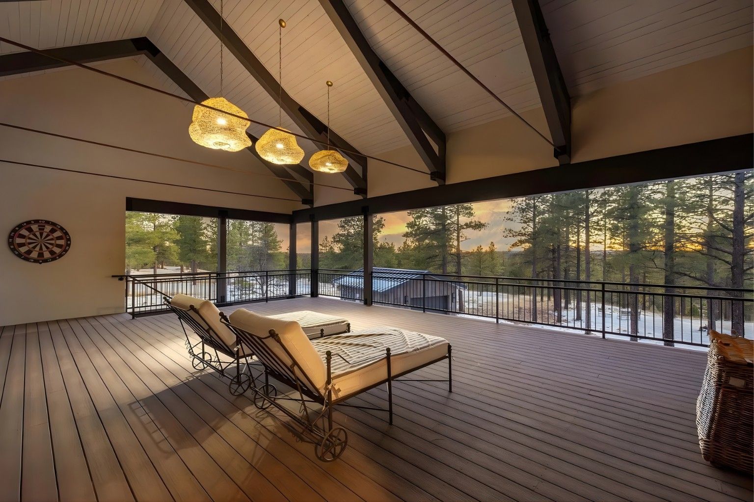 Covered patio with a lounge chair, chandelier lights, and forest views through glass railings