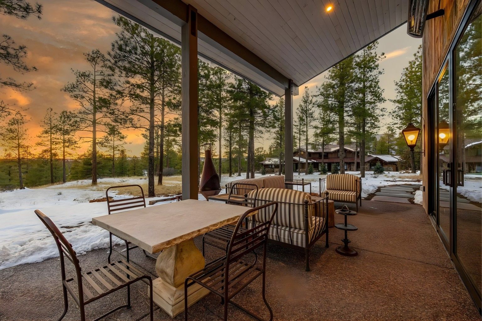 Covered patio dining area overlooking a snowy forest at sunset