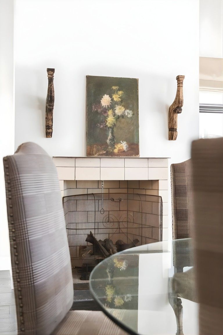 Living room fireplace with framed floral art and wall sconces above a glass table