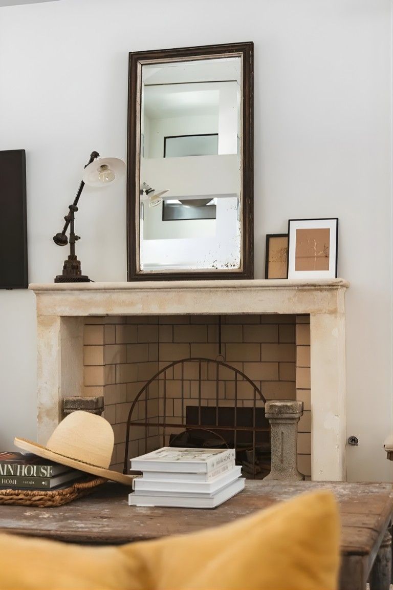 Cozy living room fireplace with mirror, lamp, books, and framed art on the mantel
