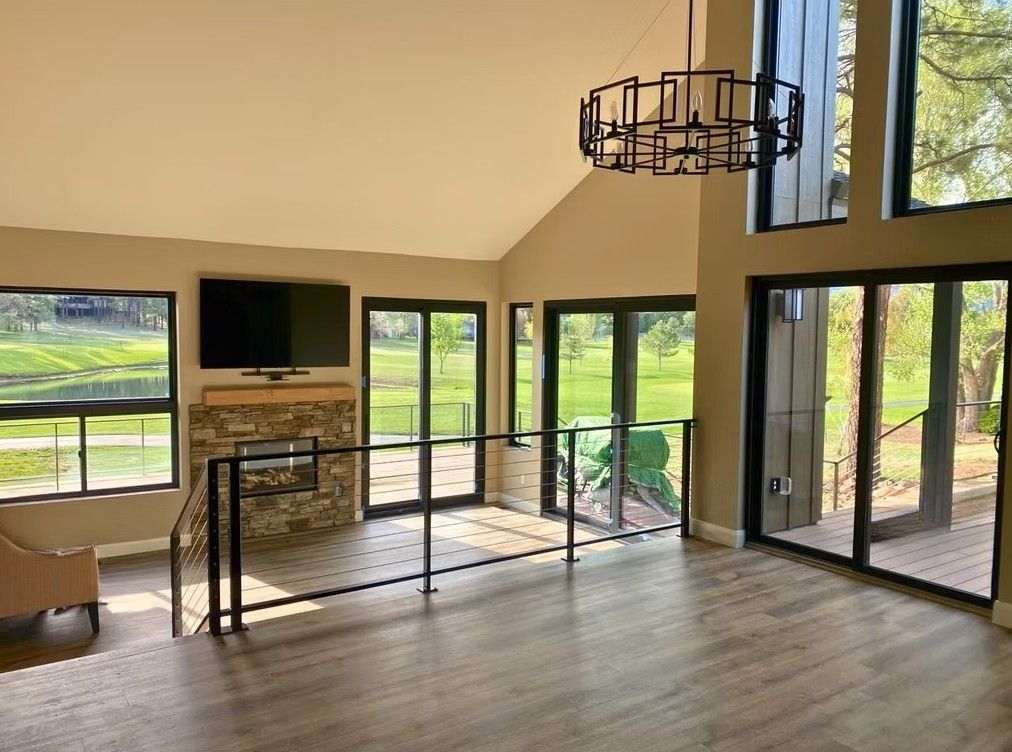 Modern living room with large windows, fireplace, TV, and stairs overlooking a green landscape
