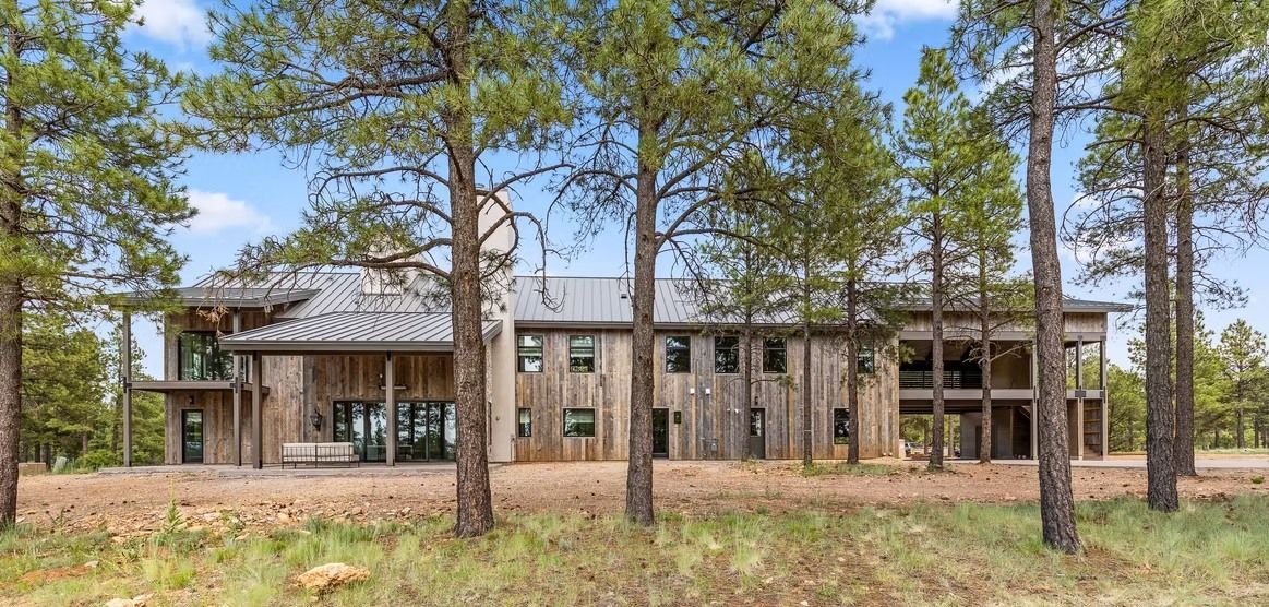 Modern two-story house with wood exterior among pine trees in a forest setting