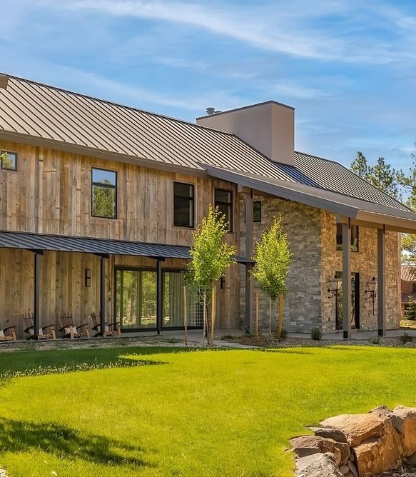 Modern two-story wooden house with stone accents, large windows, and a green lawn under a blue sky