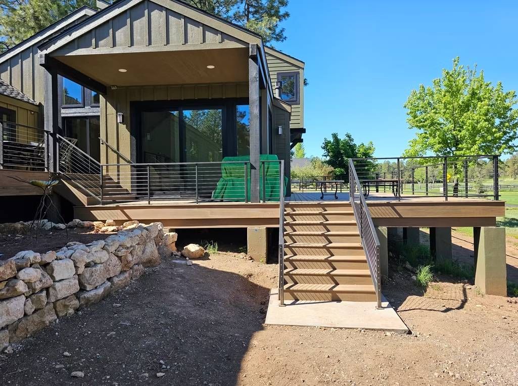 Modern house with raised deck, stairs, and stone retaining wall in a sunny yard