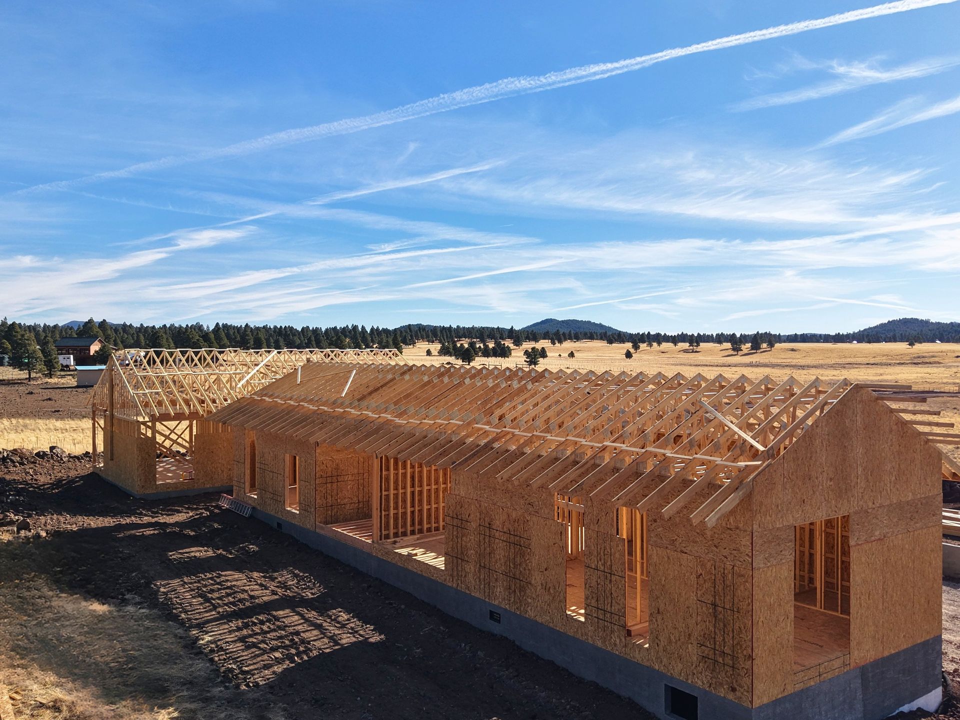 Wooden house frame under construction in an open field beneath a blue sky