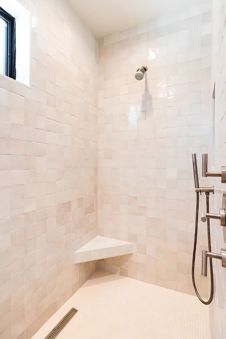 Empty tiled shower stall with a corner shelf, showerhead, and handheld sprayer