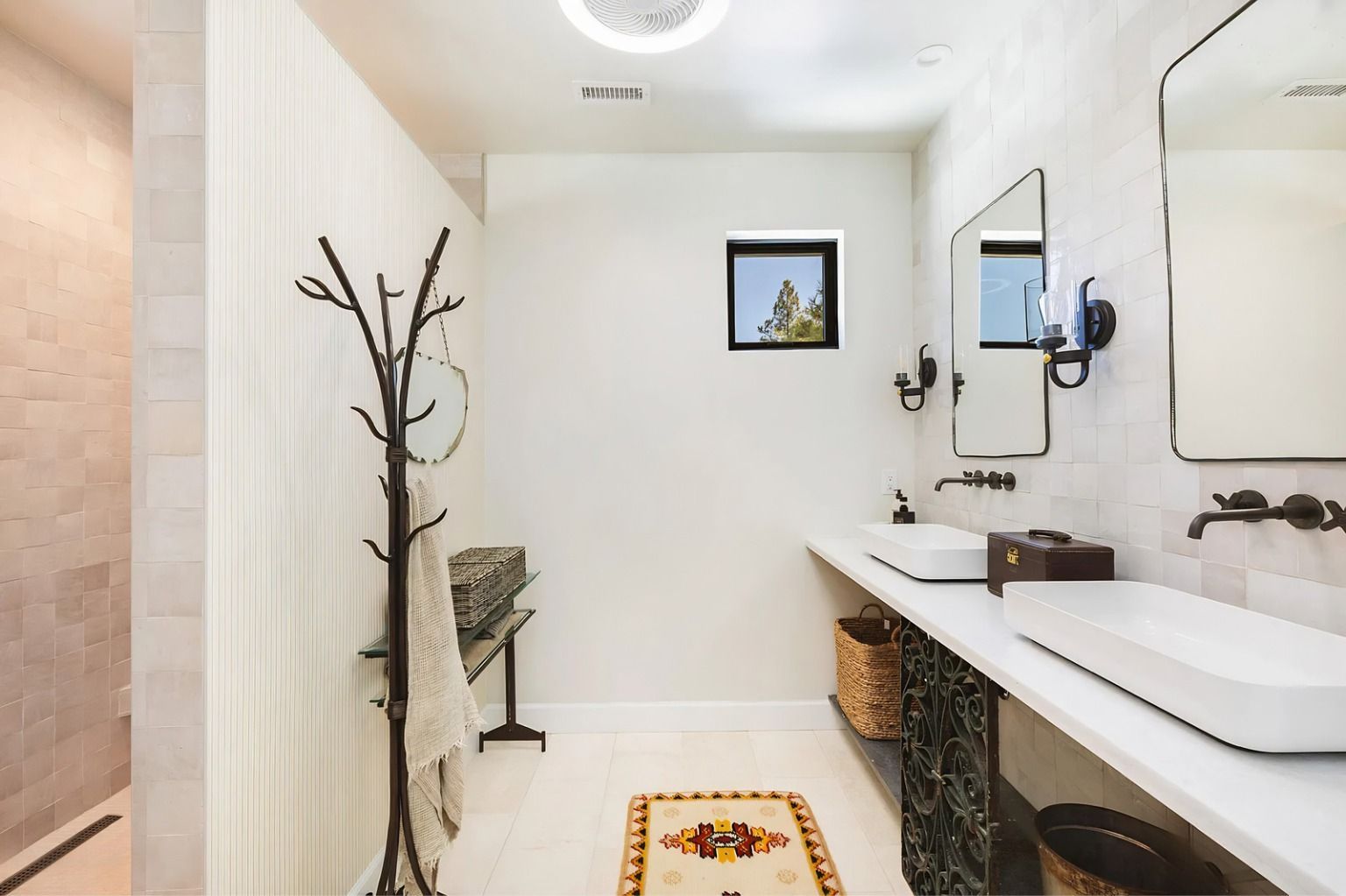 Minimal white bathroom with long sink, mirror, wall hooks, and a coat rack near the shower.