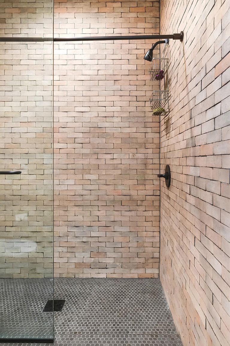Modern shower with glass wall, brick tile walls, and tiled floor with drain and fixtures