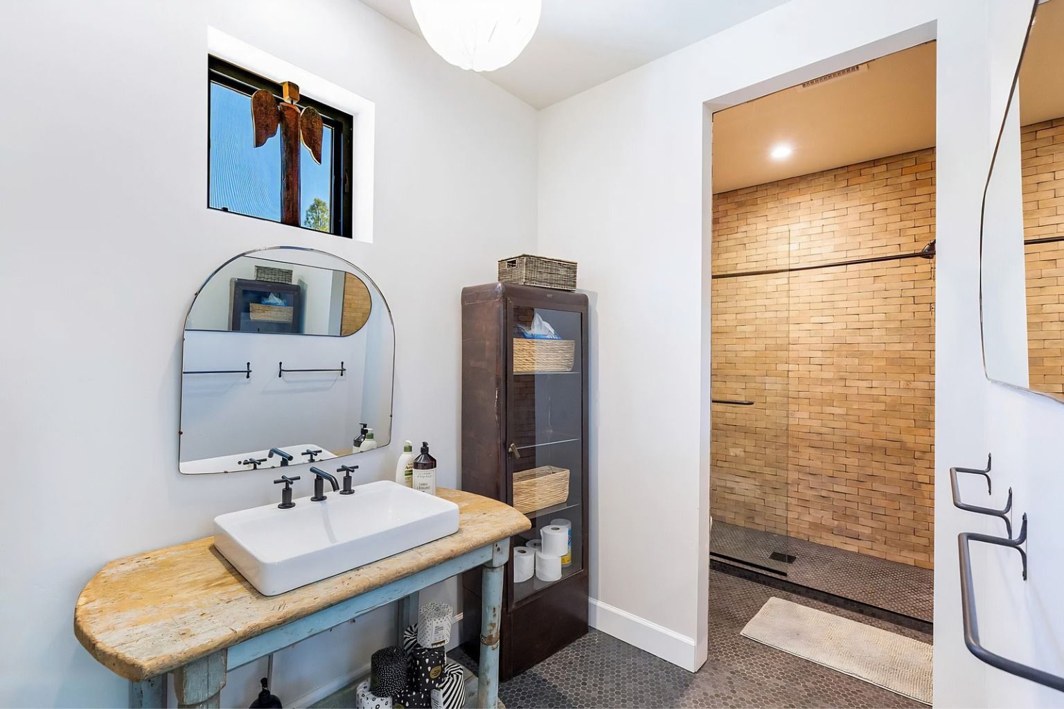 Modern bathroom vanity with sink, mirror, and a tiled walk-in shower doorway.