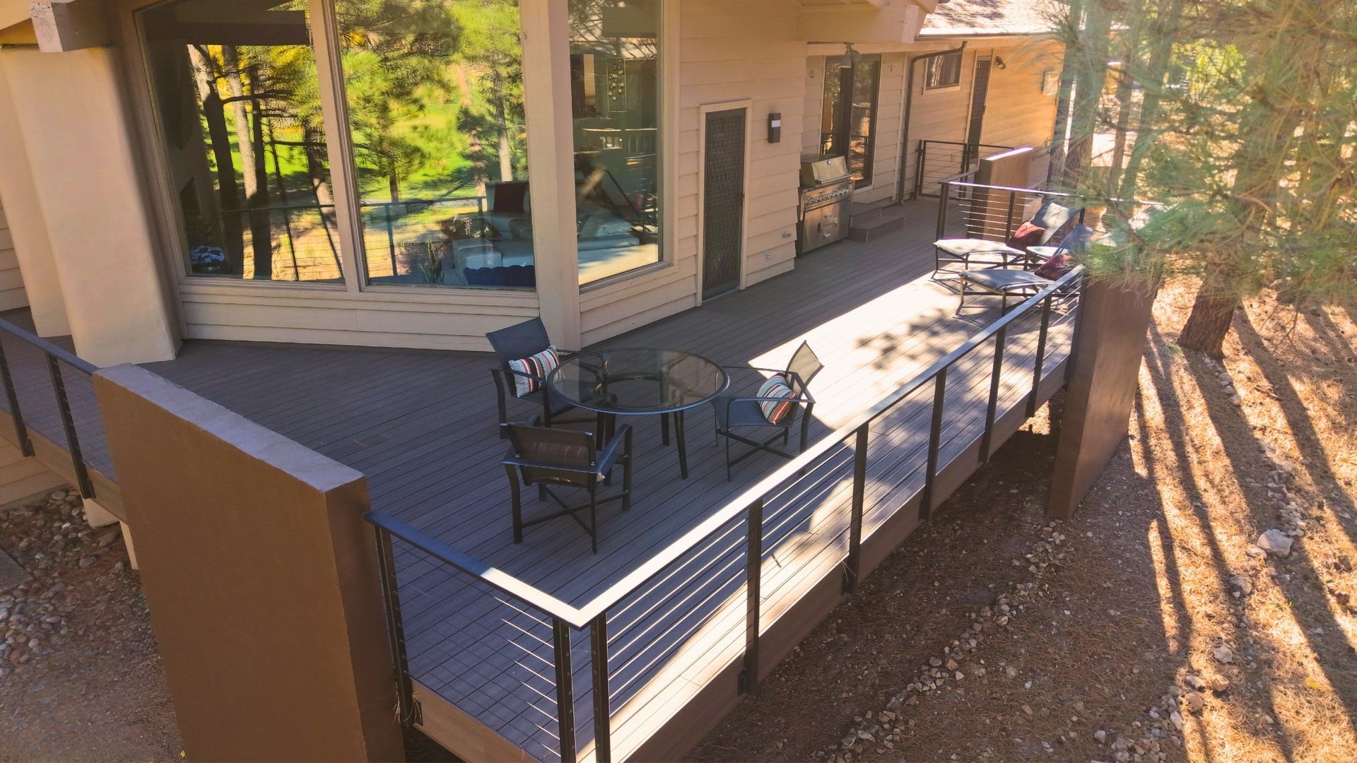 Covered patio with outdoor tables and chairs, black railing, and sunlight casting shadows over the deck.