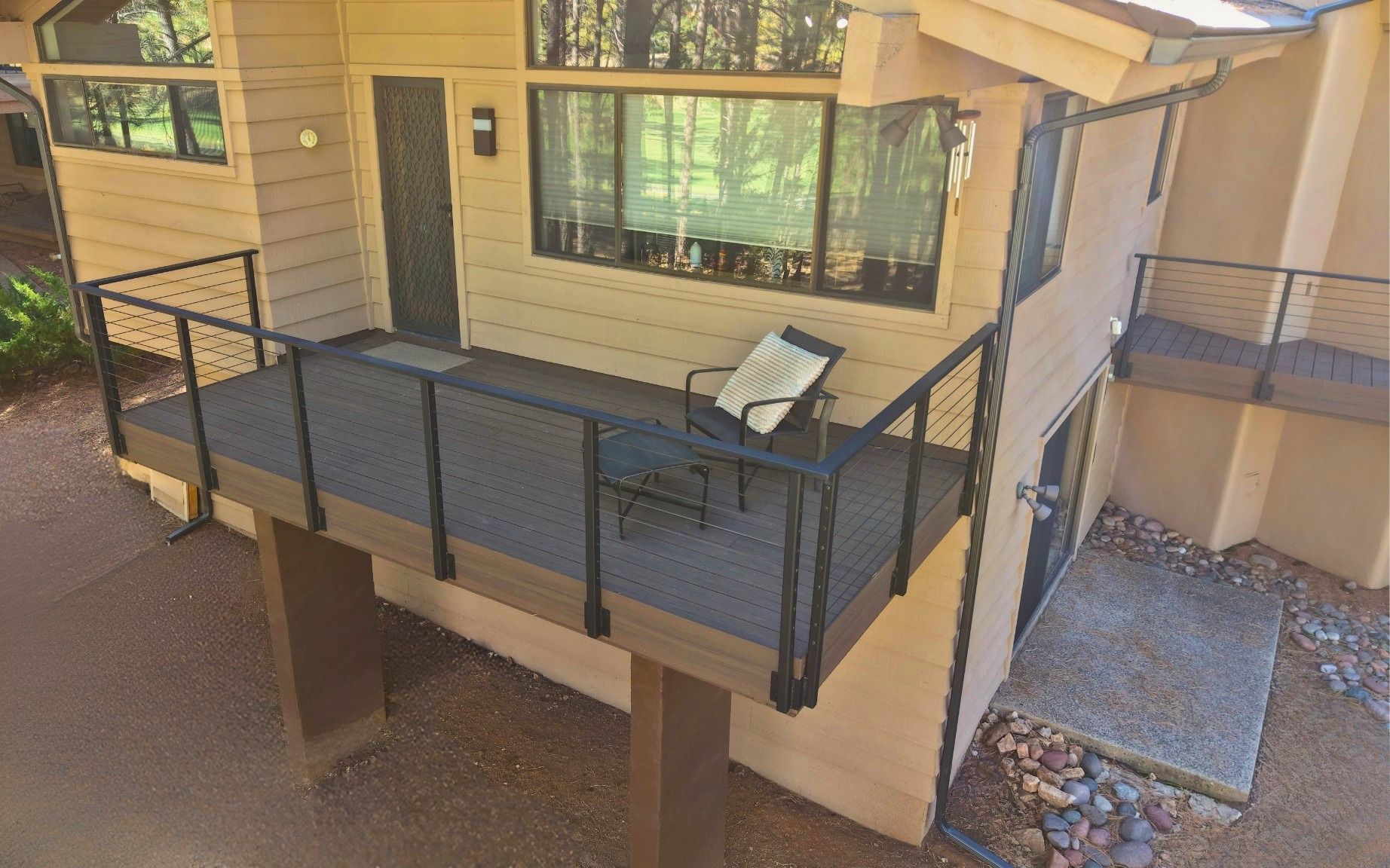 Small outdoor balcony with black railing, tan siding, and a table holding a folded chair.
