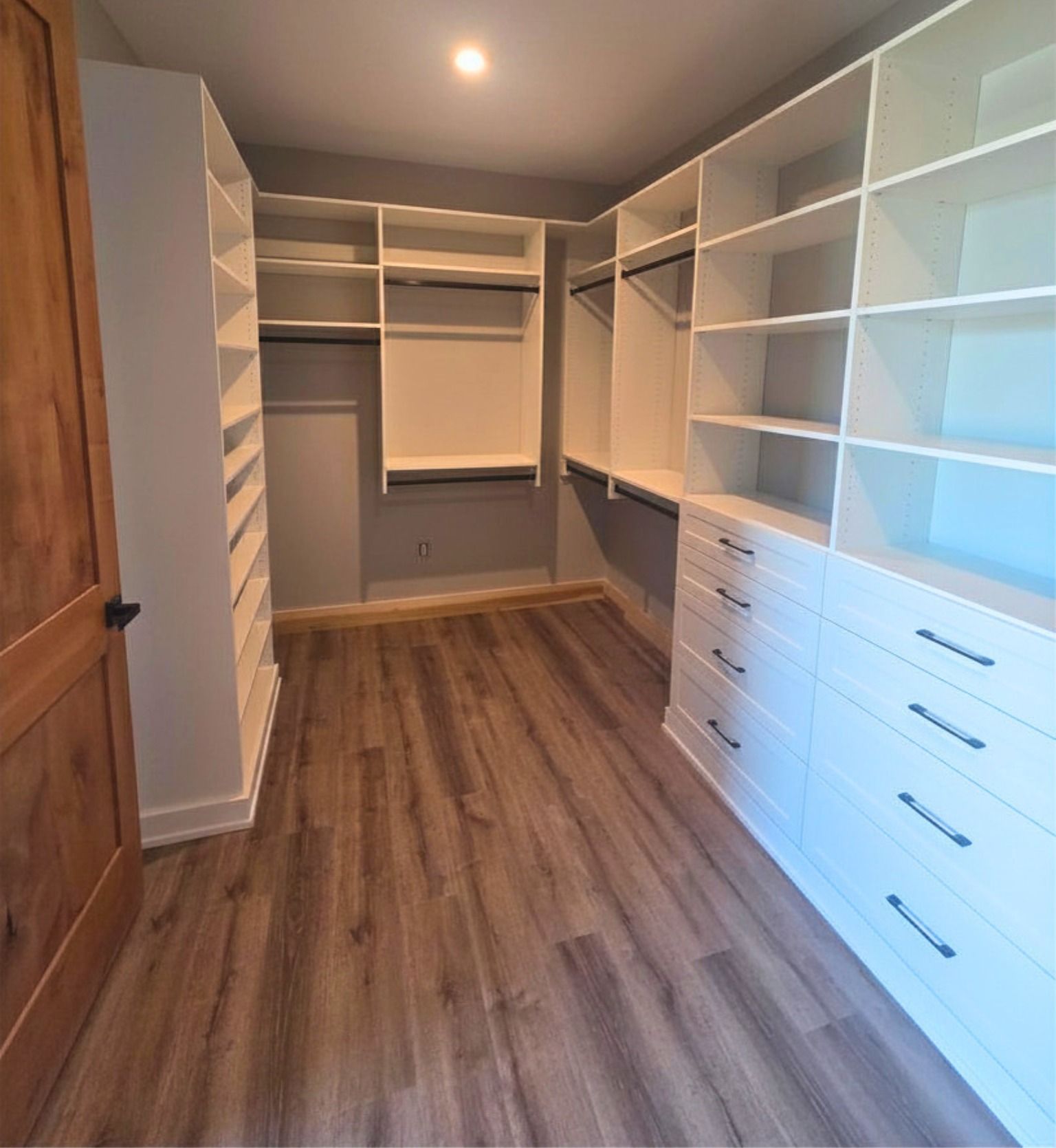 Walk-in closet with white shelving and drawers, wood floor, and gray walls.