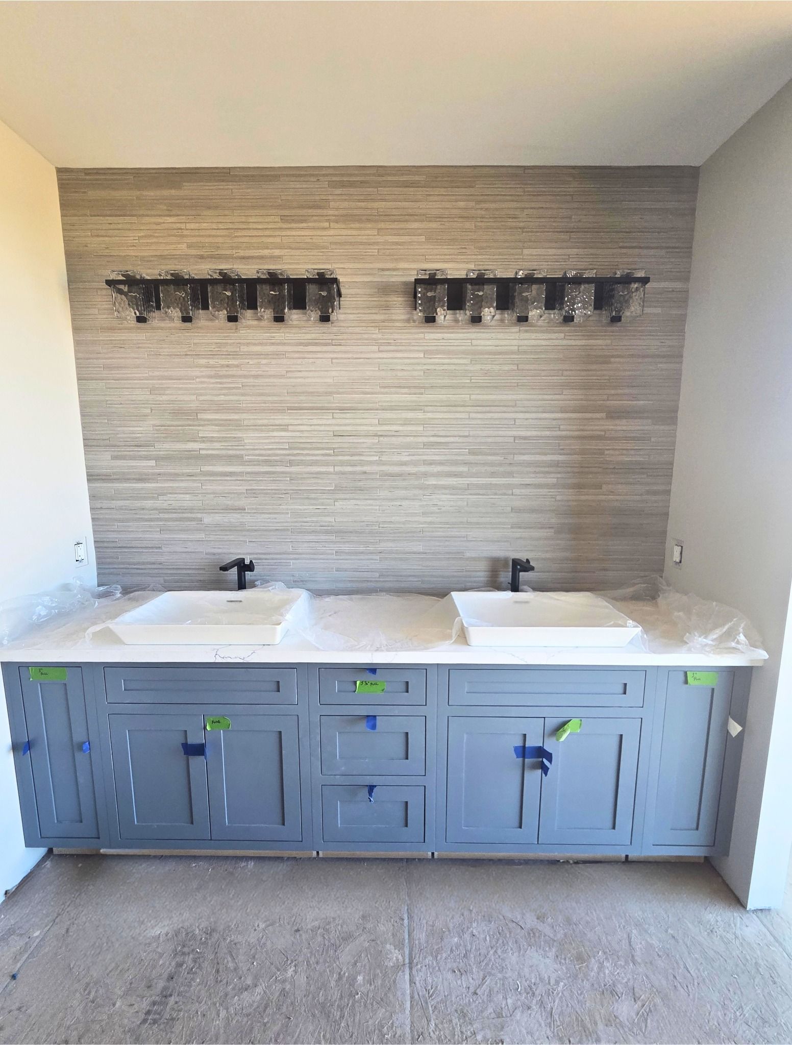 Modern bathroom vanity with dual sinks, gray cabinets, and wall-mounted faucets against a tiled backsplash.
