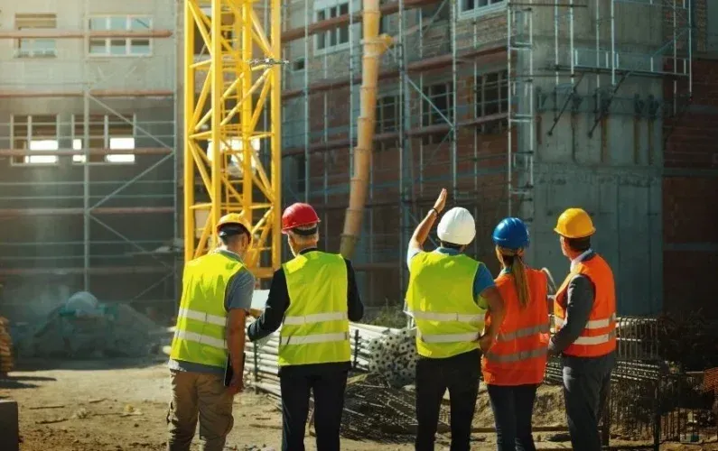 Construction workers in reflective vests and hard hats inspecting a building site with scaffolding.